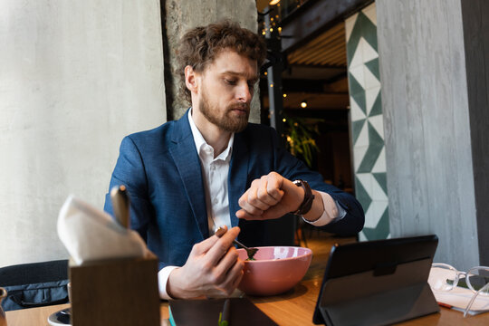 Male owner checking time while having food sitting with digital tablet at cafe