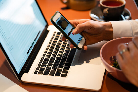 Businessman using smart phone over laptop while sitting at cafe