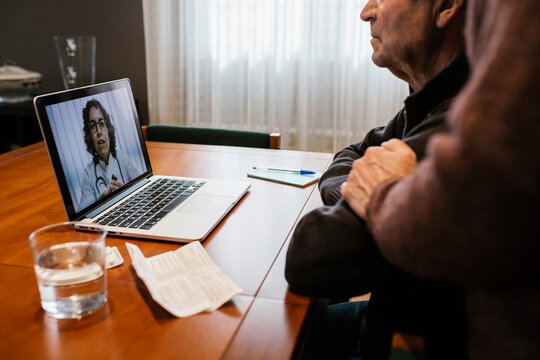 Senior man and female social worker on online consultation with female doctor at home during COVID-19