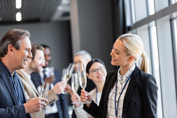 smiling interracial business people holding champagne glasses during conversation in hall