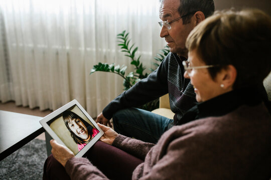 Grandparents on video call with granddaughter through digital tablet at home