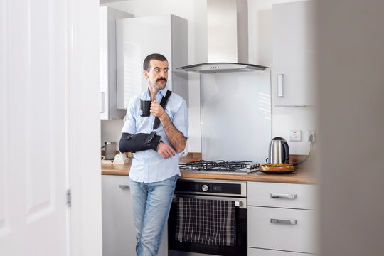 Man wearing arm sling while drinking tea in kitchen at home