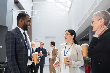 smiling multiethnic business people holding coffee to go while talking during conference