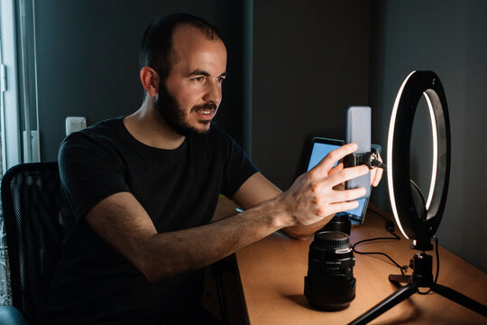 Male influencer adjusting mobile phone attached to illuminated circular strobe at studio
