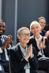 Obraz premium selective focus of middle aged businesswoman applauding near interracial colleagues on conference