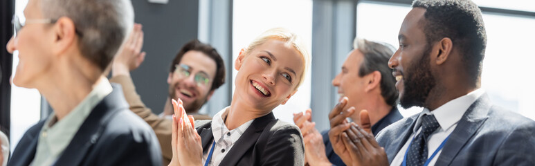 selective focus of young businesswoman applauding together with interracial colleagues during...