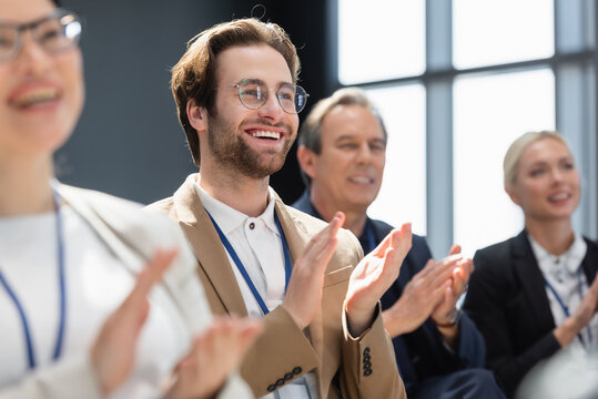 selective focus of young businessman applauding with multiethnic colleagues on seminar