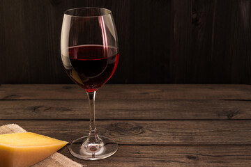 Glass of red wine with a piece of parmesan on an old wooden table. Focus on the stem glass