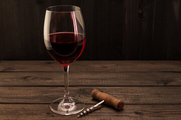 Glass of red wine and corkscrew on an old wooden table. Focus on the corkscrew