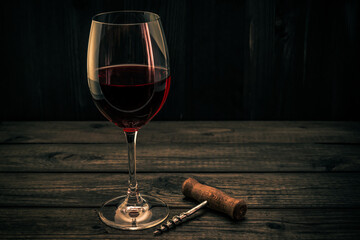 Glass of red wine and corkscrew on an old wooden table. Focus on the corkscrew