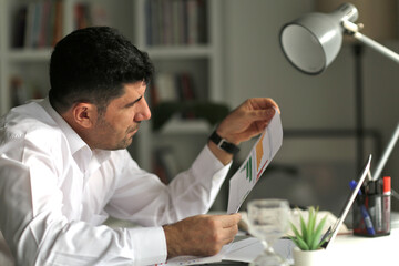 Businessman working on laptop and writing notes in living room at home.Working  on documents