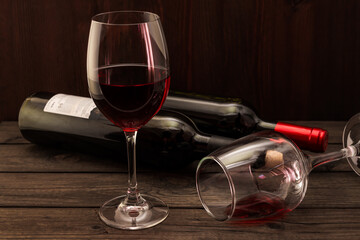 Two bottles of red wine with two glasses on an old wooden table. Focus on an overturned glass of wine
