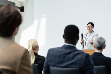 back view of blurred participants near asian lecturer pointing with hand during business conference