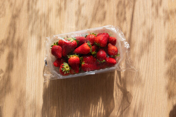 Strawberries in a plastic packaging on wooden background on a sunny day