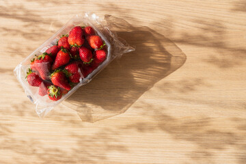 Strawberries in a plastic packaging on wooden background on a sunny day