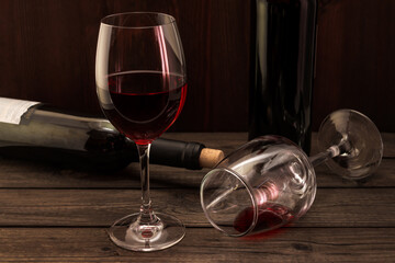 Two bottles of red wine with two glasses on an old wooden table. Focus on an overturned glass of wine
