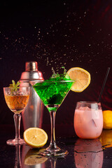 cocktail glasses with colored liquors and drinks with metal shaker with lemon and smoke in the background with the liquid flying forming a splash