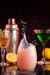 cocktail glasses with colored liquors and drinks with metal shaker with lemon and smoke in the background with the liquid flying forming a splash