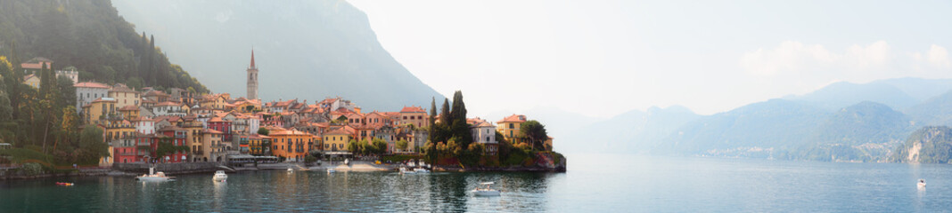 Early morning view of the Como Lake with the village of Varenna, Italy, and clear sky, with fog, soft sunlight and mountains in the distance - 433291775