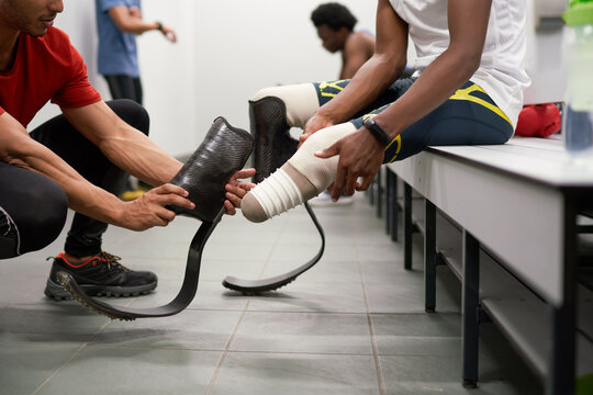 Coach helping male amputee athlete with running blade prosthetics
