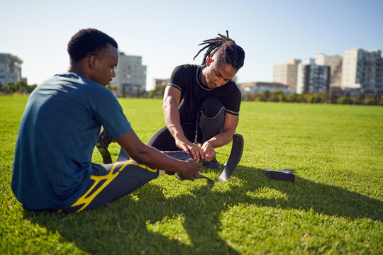 Coach helping young male amputee athlete with running blade prosthetic