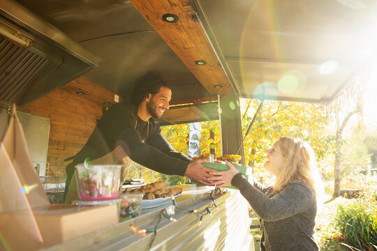 Happy food truck owner serving food to customer in sunny park