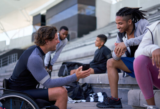 Wheelchair athlete showing smart phone to friend in stadium bleachers