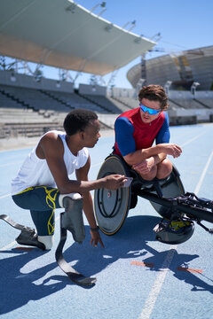 Male amputee and wheelchair athletes talking on sunny sports track