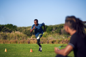 Coach watching young male amputee athlete running drills in park