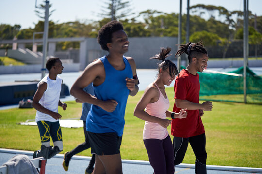 Smiling track and field athletes running on sunny sports track