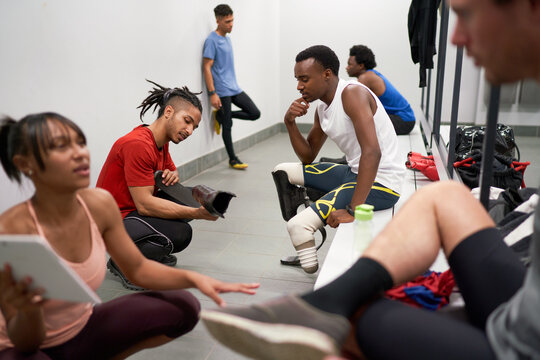 Coach with running blade prosthetic talking to athlete in locker room - Powered by Adobe