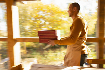 Male pizzeria owner carrying pizza boxes along sunny autumn window