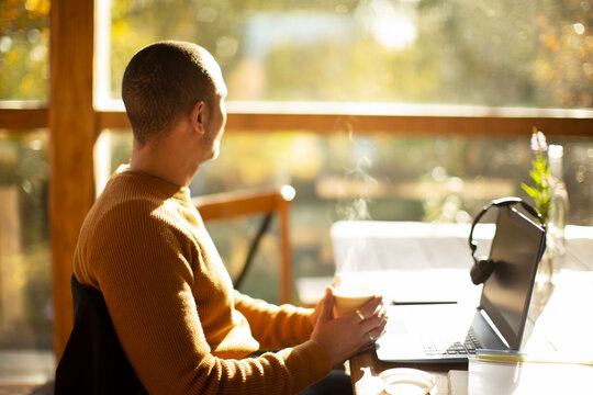 Thoughtful businessman with coffee and laptop looking out sunny window