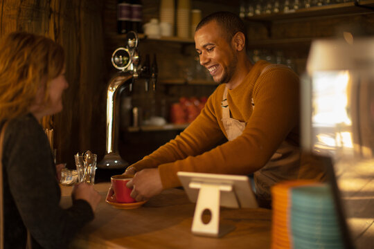 Friendly barista serving coffee to excited woman at cafe counter