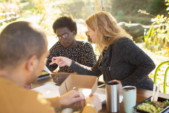 Businesswomen discussing paperwork and eating lunch at table in park