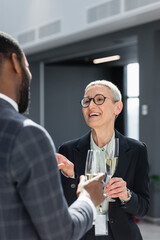 smiling middle aged businesswoman with champagne glass talking to african american colleague