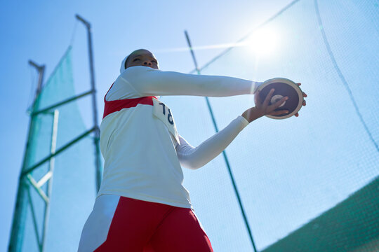 Female track and field athlete throwing discus under sunny blue sky