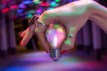 Close up hand holding light bulb under neon light