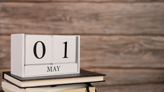 Cube wooden calendar on a pile of books, on first day of May wooden background.