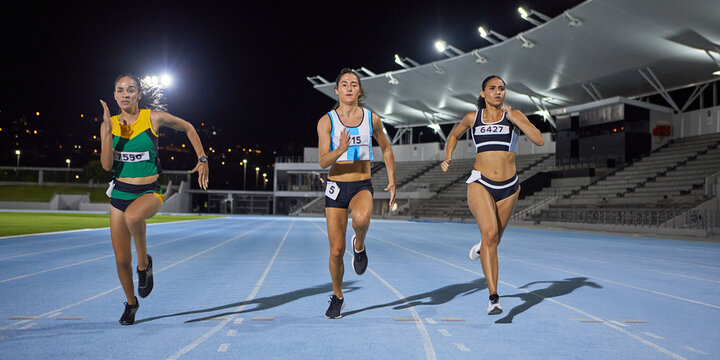 Female track and field athletes running in competition on night track
