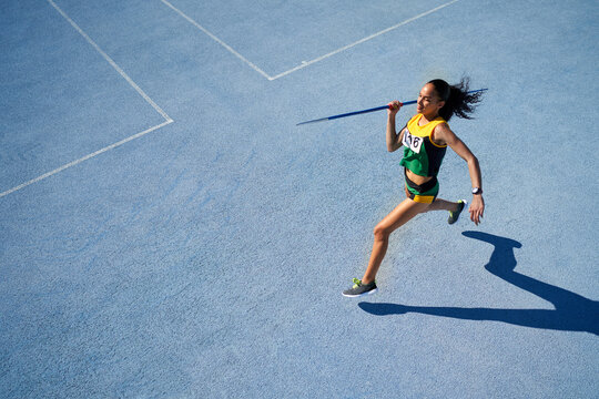 Female track and field athlete throwing javelin on sunny blue track