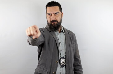 Bearded detective with police badge and serious face looking and pointing finger at the camera. Crime concept.