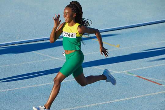 Smiling female track and field athlete running on sunny track