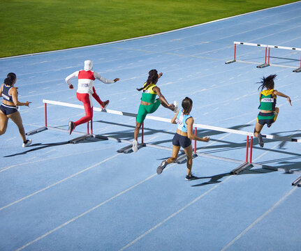 Female track and field athletes jumping hurdles in competition