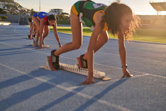 Female track and field athletes at starting blocks on sunny track