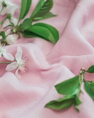 Spring background with white flowers and green leaves on a silk pink background with copy space.
The concept of a festive gentle background.Blurred 
