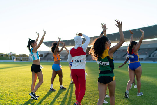 Track and field athletes waving to audience in stadium infield