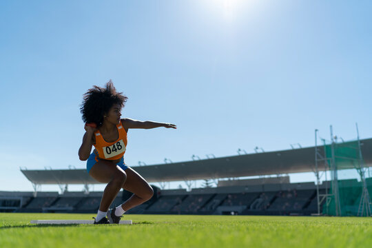 Female track and field athlete throwing shot put in sunny stadium