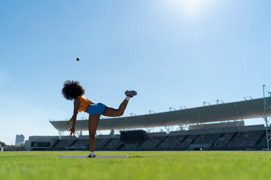 Female track and field athlete throwing shot put in sunny stadium