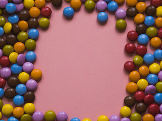 Top view of colorful chocolate candy with a frame in the center. Pink background